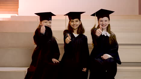Zoom-In-Of-Happy-Kindergarten-Students-In-Cap-And-Gown-Looking-At-The-Camera-And-Doing-Thumb-Up-Sign-During-The-Preschool-Graduation-Ceremony-2