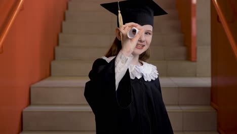 Feliz-Estudiante-De-Preescolar-Con-Toga-Y-Birrete-Bailando-Y-Jugando-Con-Diploma-De-Graduación-Mientras-Mira-La-Cámara