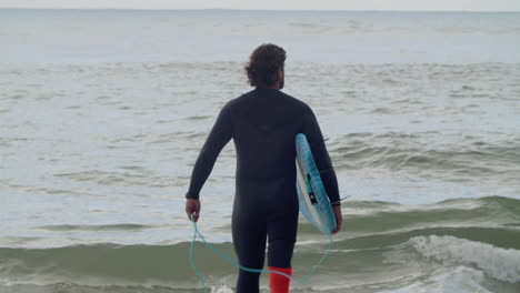 Back-View-Of-A-Man-With-Artificial-Leg-In-Wetsuit-And-Surfboard-Walking-Into-The-Ocean