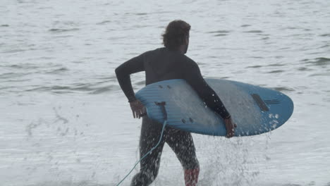 Back-View-Of-A-Man-With-Artificial-Leg-In-Wetsuit-Entering-Into-Ocean-And-Lying-On-The-Surfboard