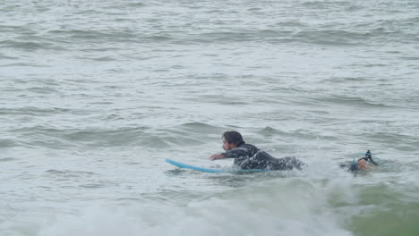Sportive-Man-In-Wetsuit-With-Artificial-Leg-Lying-On-Surfboard-And-Swimming-In-The-Ocean-2