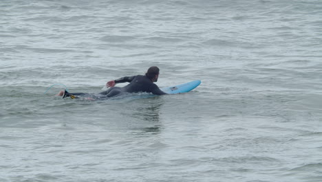 Sportive-Man-In-Wetsuit-With-Artificial-Leg-Lying-On-Surfboard-And-Swimming-In-The-Ocean-3