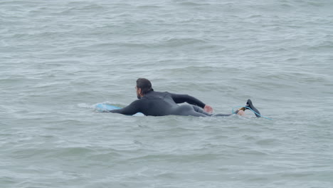 Sportive-Man-In-Wetsuit-With-Artificial-Leg-Lying-On-Surfboard-And-Swimming-In-The-Ocean-4