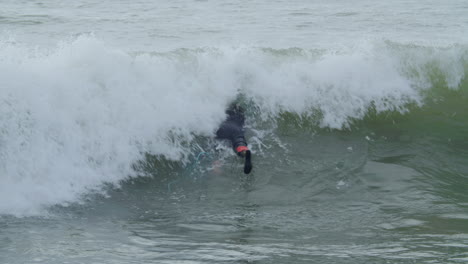 Sportive-Man-In-Wetsuit-With-Artificial-Leg-Lying-On-Surfboard-And-Swimming-In-The-Ocean-When-A-Wave-Covering-Him-1