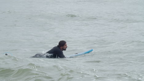 Sportive-Man-In-Wetsuit-With-Artificial-Leg-Lying-On-Surfboard-And-Swimming-In-The-Ocean-6