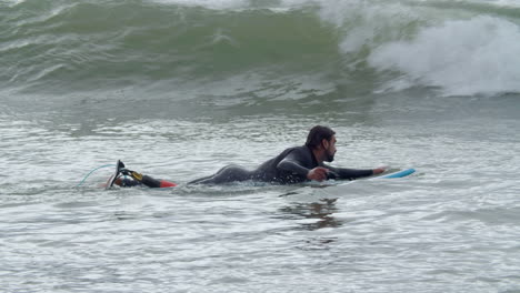 Sportive-Man-In-Wetsuit-With-Artificial-Leg-Lying-On-Surfboard-And-Swimming-In-The-Ocean-When-A-Wave-Covering-Him-2