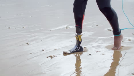 Close-Up-Of-An-Unrecognizable-Man-In-Wetsuit-With-Bionic-Leg-Walking-Along-The-Seashore