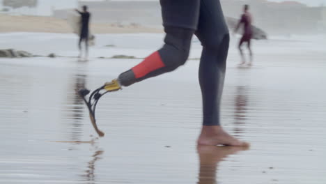 Nahaufnahme-Eines-Nicht-Erkennbaren-Surfers-Im-Neoprenanzug-Mit-Bionischem-Bein,-Der-Ins-Meer-Läuft