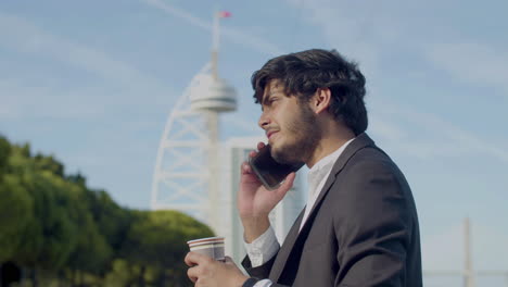 Feliz-Hombre-De-Negocios-árabe-Con-Traje,-Bebiendo-Café-Y-Hablando-Por-Teléfono-Al-Aire-Libre