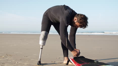 Vertikale-Bewegung-Eines-Männlichen-Surfers-Mit-Beinprothese,-Die-Leine-Auf-Surfbrett-Bindet
