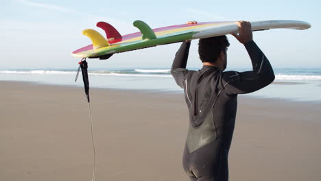 Rückansicht-Eines-Männlichen-Surfers-Mit-Beinprothese,-Der-Mit-Einem-Surfbrett-Auf-Dem-Kopf-Am-Strand-Spazieren-Geht