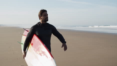 Medium-Shot-Of-A-Male-Surfer-With-Artificial-Leg-Walking-Along-Beach-And-Holding-Surfboard-Under-Arm