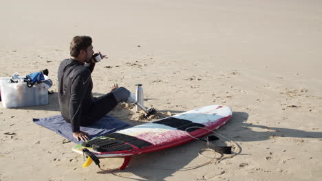 Static-Shot-Of-A-Male-Surfer-With-Artificial-Leg-Drinking-Tea-On-Beach