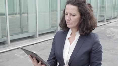 Dolly-Shot-Of-A-Focused-Businesswoman-In-Suit-Using-Tablet-For-Work-While-Walking-Outside