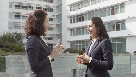 Two-Smiling-Business-Ladies-Standing-Outside-Office-Building,-Talking-And-Gesturing-With-Hands