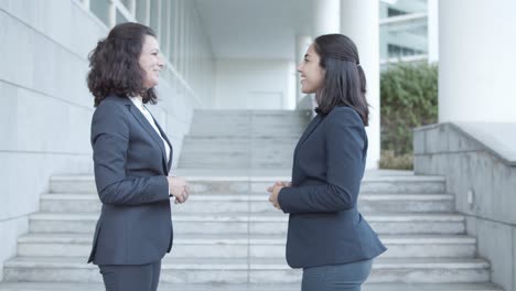 Side-View-Of-Two-Friendly-Female-Office-Colleagues-In-Suits-Meeting-Outside,-Shaking-Hands-And-Talking