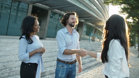 Successful-Young-Businessman-Shaking-Hands-With-Female-Partner-With-Business-Assistant-Standing-Nearby