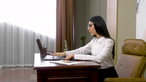 Mujer-De-Negocios-Seria-Que-Trabaja-En-Una-Computadora-Portátil-Y-Luego-Escribe-En-La-Agenda-Mientras-Está-Sentada-En-El-Escritorio-De-La-Oficina