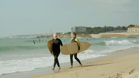 Senior-Couple-In-Wetsuit-Walking-Along-The-Beach-With-Surfboard-And-Holding-Hands