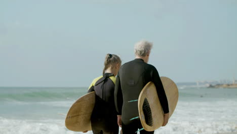 Back-View-Of-A-Senior-Couple-In-Wetsuit-Walking-Along-The-Beach-With-Surfboard-1
