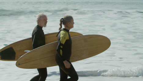 Senior-Couple-In-Wetsuit-Holding-Surfboard-And-Running-Into-The-Ocean