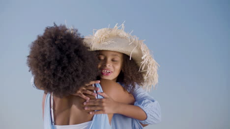 Happy-Girl-In-Straw-Hat-Running-To-Her-Mum,-Hugging-And-Kissing-Her-At-The-Beach
