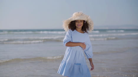 Glückliches-Mädchen-Mit-Strohhut-Und-Blauem-Kleid,-Das-Am-Strand-Tanzt