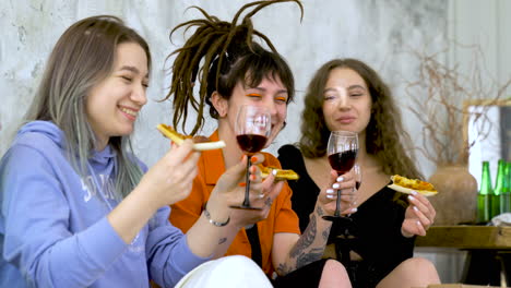 Happy-Female-Friends-Eating-Pizza-And-Toasting-With-Wine-At-Home
