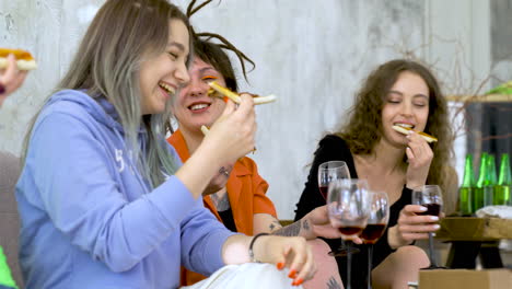 Happy-Female-Friends-Eating-Pizza,-Drinking-Wine-And-Talking-At-Home