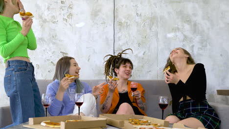 Happy-Female-Friends-Eating-Pizza,-Drinking-Wine-And-Talking-At-Home-1