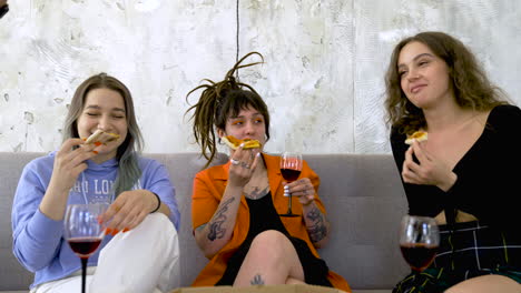 Happy-Woman-With-Tattoos-And-Dreadlocks-Eating-Pizza-And-Drinking-Wine-While-Talking-With-Friends-At-Home