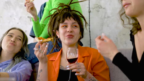 Happy-Woman-With-Tattoos-And-Dreadlocks-Eating-Pizza-And-Drinking-Wine-While-Talking-With-Friends-At-Home-1