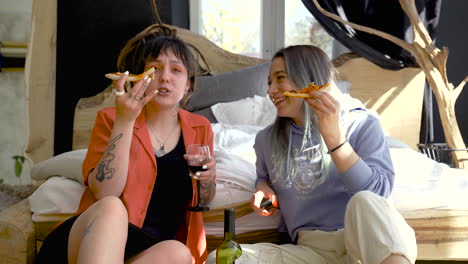 Front-View-Of-Two-Happy-Girls-Drinking-Wine-And-Eating-Pizza-While-Sitting-On-The-Floor-And-Watching-Tv-1