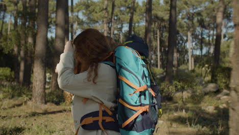 Side-View-Of-Two-Female-Friends-With-Backpacks-Hiking-Together-In-The-Forest-On-A-Sunny-Day