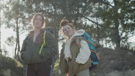 Two-Young-Female-Backpackers-Looking-At-The-Camera-And-Smiling-While-Hiking-In-The-Forest-On-A-Sunny-Day