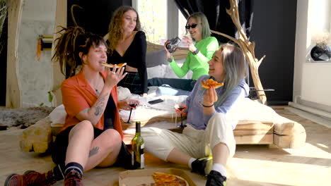 Two-Happy-Girls-Eating-Pizza-On-The-Floor-While-Their-Two-Friends-Sitting-On-The-Bed-And-One-Of-Them-Recording-With-Video-Camera