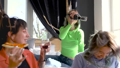 Hipster-Blonde-Girl-Sitting-On-The-Bed-And-Recording-A-Video-Of-Her-Friends-Who-Drinking-Wine-And-Eating-Pizza-At-Home