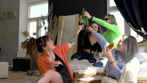 Group-Of-Four-Young-Female-Friends-Toasting-With-Beers-And-Wine-While-Eating-Pizza-At-Home-1