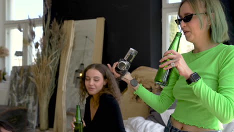 Hipster-Blonde-Girl-Sitting-On-The-Bed-And-Recording-A-Video-Of-Her-Friends-During-A-Party-At-Home