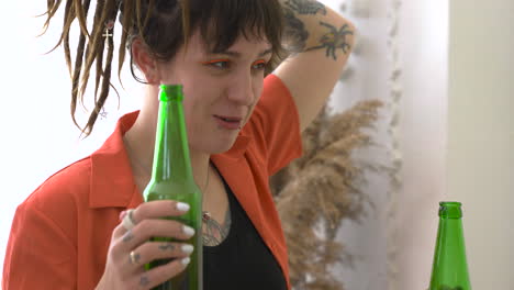 Close-Up-Of-A-Young-Woman-With-Dreadlocks-And-Tattoos-Drinking-Beer-And-Talking-With-Her-Friends-During-A-Party-At-Home