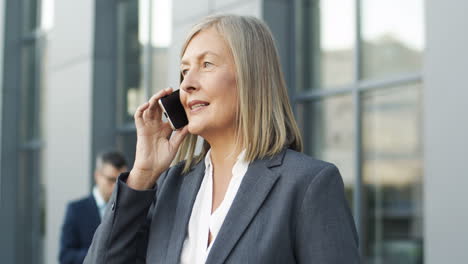 Close-Up-View-Of-Mature-Businesswoman-Talking-On-The-Phone-In-The-Street
