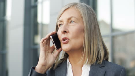 Close-Up-View-Of-Mature-Businesswoman-Talking-On-The-Phone-In-The-Street-1
