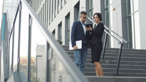 Distant-View-Of-Businesswoman-Showing-Something-To-Businessman-On-Tablet-Device-While-They-Standing-On-Steps