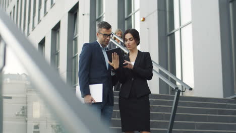 Distant-View-Of-Businesswoman-Showing-Something-To-Businessman-On-Tablet-Device-While-They-Standing-On-Steps-1