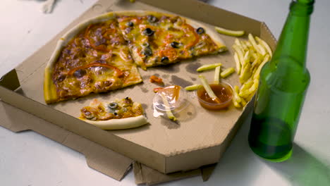 Delicious-Pizza-With-Black-Olives-And-Red-Peppers,-French-Fries-With-Tomate-Sauce-And-Empty-Beer-Bottle