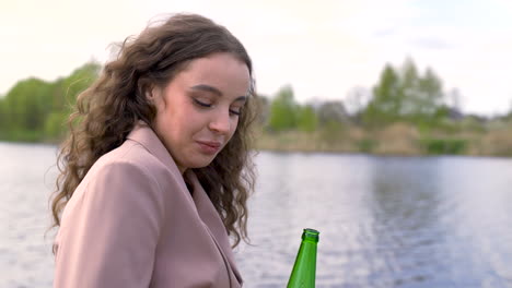 Happy-Curly-Brunette-Woman-Talking-With-Her-Friend-And-Drinking-Beer-On-The-Riverside
