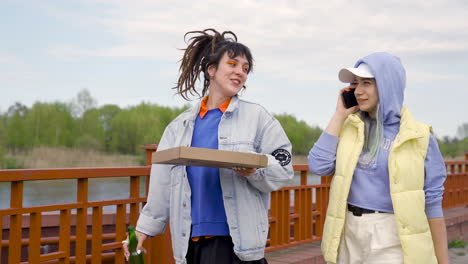 Young-Woman-With-Dreadlocks-Drinking-Beer-And-Holding-Pizza-Box-While-Her-Friend-Talks-On-The-Phone