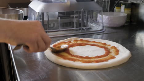 Close-Up-View-Of-A-Chef-Hands-Spreading-Sauce-On-Pizza-Dough-On-A-Restaurant-Kitchen-Countertop