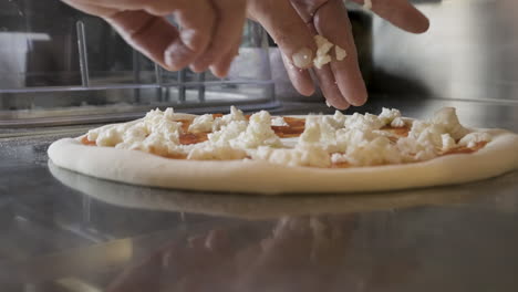 Close-Up-View-Of-A-Chef-Hands-Spreading-Cheese-On-Pizza-Dough-On-A-Restaurant-Kitchen-Countertop