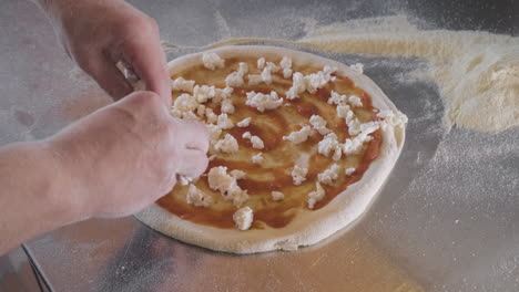 Close-Up-View-Of-A-Chef-Spreading-Cheese-On-Pizza-Dough-On-A-Restaurant-Kitchen-Countertop